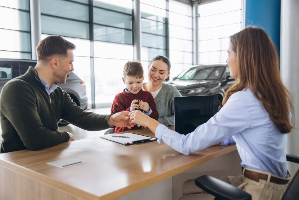Conseillère en assurances remettant les clés d'un véhicule à une famille dans une concession automobile.