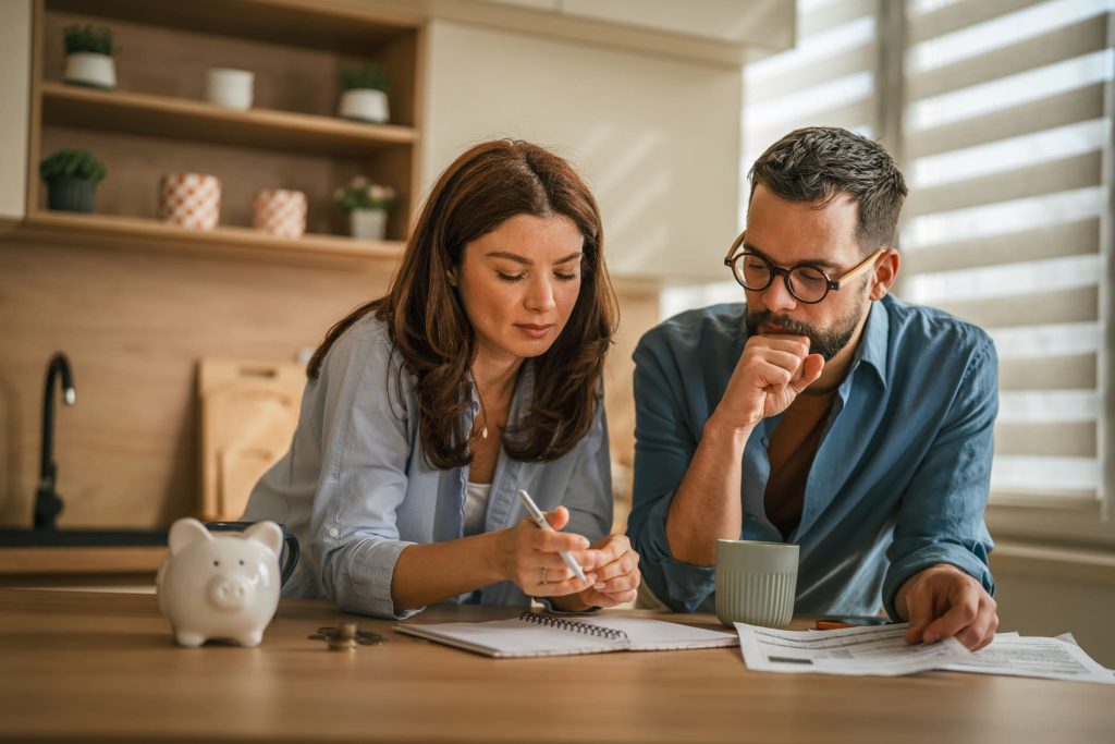 Couple analysant son budget et ses finances à domicile avec des documents et un carnet de notes.