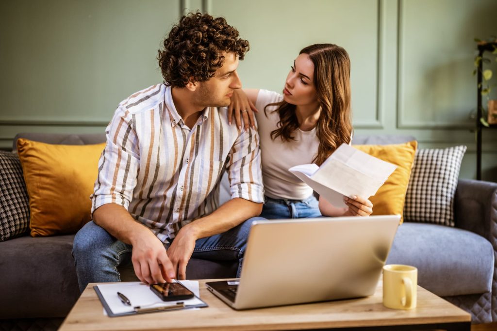 Jeune couple analysant des documents financiers et son budget à domicile avant de souscrire un crédit.