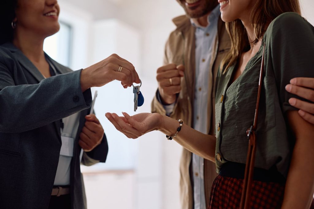 Conseillère remettant les clés d'une maison à un couple, symbolisant l'accompagnement dans un projet immobilier et un prêt hypothécaire.