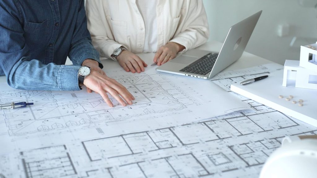 Couple étudiant les plans d'une future construction avec un ordinateur portable, illustrant un projet de crédit construction.