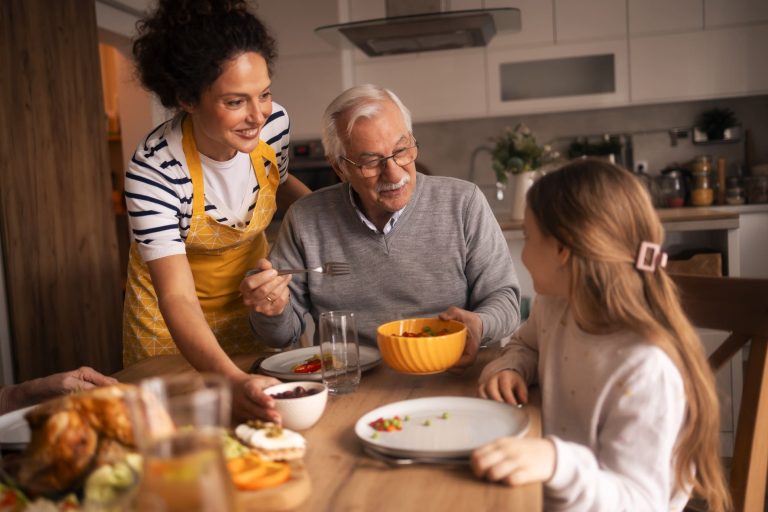 Famille réunie autour d'un repas avec un grand-parent, illustrant une assurance familiale et la protection de vos proches.
