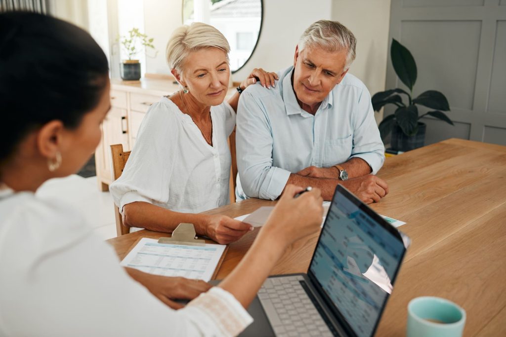 Couple échangeant avec un conseiller financier au sujet d'un prêt, autour d'une table avec des documents et un ordinateur portable.