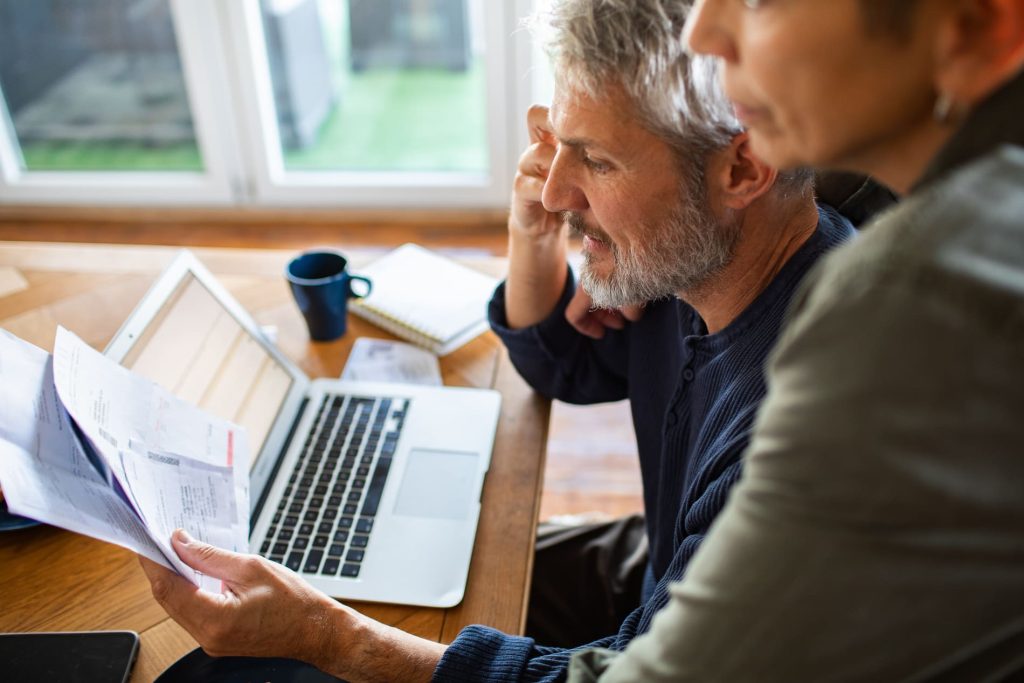 Couple analysant ses documents financiers avec un ordinateur portable, illustrant un projet de rachat de crédits.
