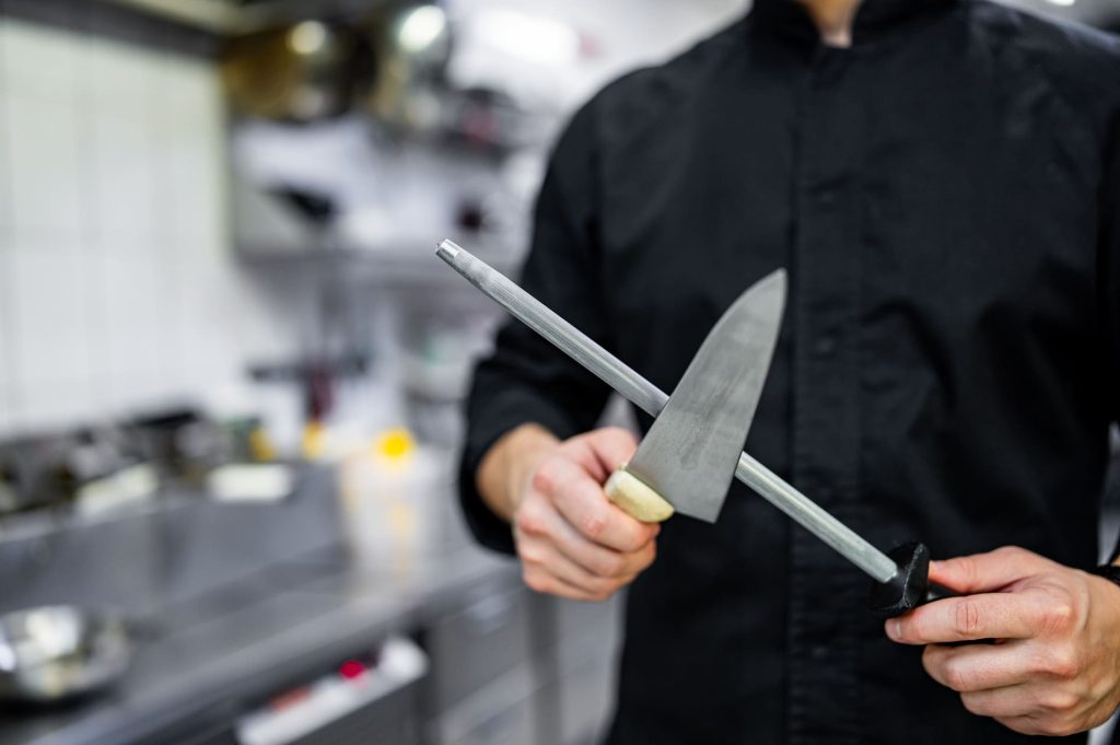 Professionnel aiguisant un couteau en cuisine, illustrant les assurances spécifiques pour les métiers de bouche et les activités professionnelles.