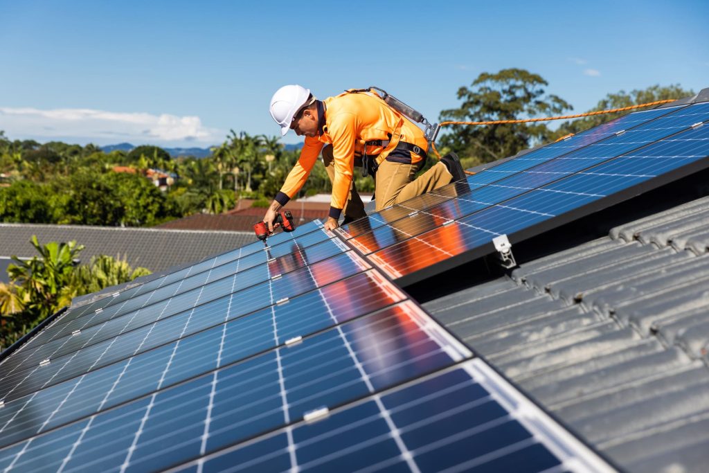 Technicien installant des panneaux photovoltaïques sur une toiture, illustrant des travaux de rénovation énergétique.